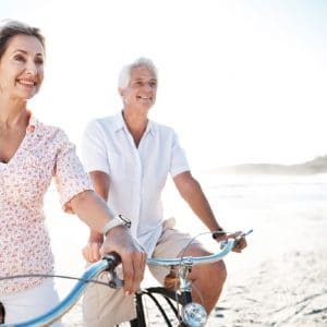 A senior couple riding their bikes together on the beach